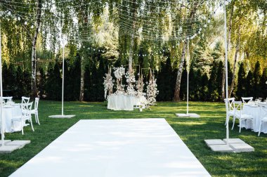 Yeni evliler için düğün masası. Beyaz tabaklar ve peçetelerle süslenmiş şölen masası, yeşillik ve çiçekler ve mumlar, açık havada.