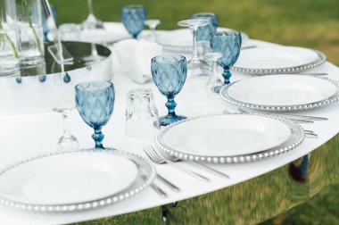 Açık hava düğün ziyafeti. Masa beyaz tabaklar ve şarap için özel bardaklarla süslenmiştir..