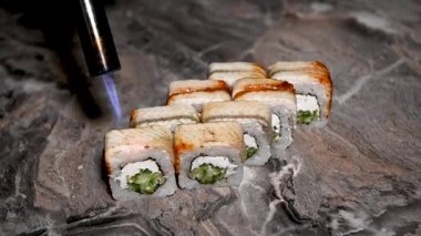 Philadelphia usulü suşi pişirme işlemi yakın çekim. Suşi ustası ruloyu keskin bir bıçakla parçalara ayırıyor. Geleneksel Japon yemekleri ve deniz ürünleri..
