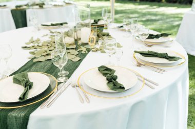 Açık hava düğün ziyafeti. Masa beyaz tabaklar ve şarap için özel bardaklarla süslenmiştir..