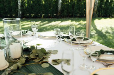 Açık hava düğün ziyafeti. Masa beyaz tabaklar ve şarap için özel bardaklarla süslenmiştir..
