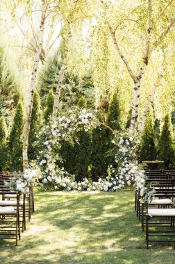 Beyaz çiçekler ve açık hava yeşilliği ile süslenmiş daire şeklinde düğün kemeri. Düğün hazırlığı. Çiçek bileşimi