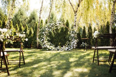 Beyaz çiçekler ve açık hava yeşilliği ile süslenmiş daire şeklinde düğün kemeri. Düğün hazırlığı. Çiçek bileşimi