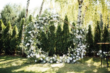 Beyaz çiçekler ve açık hava yeşilliği ile süslenmiş daire şeklinde düğün kemeri. Düğün hazırlığı. Çiçek bileşimi