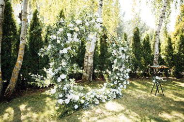 Beyaz çiçekler ve açık hava yeşilliği ile süslenmiş daire şeklinde düğün kemeri. Düğün hazırlığı. Çiçek bileşimi