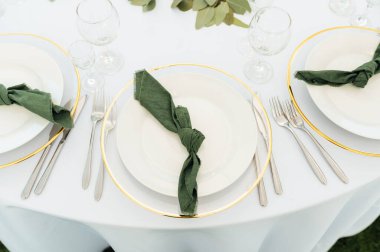 Açık hava düğün ziyafeti. Masa beyaz tabaklar ve şarap için özel bardaklarla süslenmiştir..