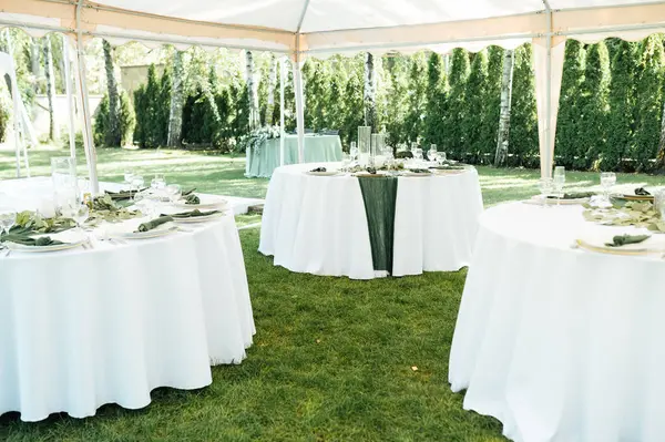 オープン エアウェディングバンケット テーブルはワインのための白い版そしてプレミアム メガネによって飾られます ストック写真