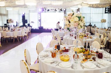 Düğün için. Ziyafet. Sandalyeler ve yuvarlak masa misafirler için çatal bıçak takımı, yeşillik çiçekleri ve çanak çömlek ile servis ediliyor ve beyaz bir masa örtüsüyle kaplanıyor. zeytin rengi