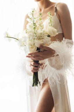 Gelinin sabahında, beyaz ipek bornoz giyen bir kadın bir düğün buketi tutuyor. Yakın plan fotoğraf. Gelinin düğün gününün sabahı.