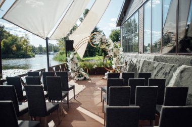 Açık hava seremonisi için modern alan. Misafirler için koyu sandalyeli yuvarlak kemer ve güneş örtüsü..