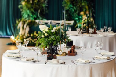 Lüks restoran. Lüks içecekler, beyaz masalar, konuklara servis tabakları ve bardaklar. Dekor yeşilden yapılmıştır. Zümrüt rengi