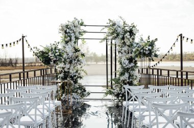 Çiçeklerle süslenmiş bir düğün kemeri, bir podyumda duruyor, açık havada duruyor, nehrin zeminine karşı yapılacak tören için. Fotoğraf, tatil tasarımı konsepti.