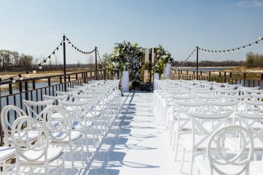 Çiçeklerle süslenmiş bir düğün kemeri, bir podyumda duruyor, açık havada duruyor, nehrin zeminine karşı yapılacak tören için. Fotoğraf, tatil tasarımı konsepti.