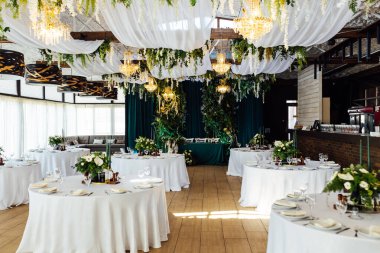 Lüks restoran. Lüks içecekler, beyaz masalar, konuklara servis tabakları ve bardaklar. Dekor yeşilden yapılmıştır. Zümrüt rengi