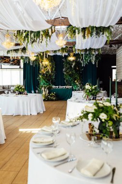 Lüks restoran. Lüks içecekler, beyaz masalar, konuklara servis tabakları ve bardaklar. Dekor yeşilden yapılmıştır. Zümrüt rengi