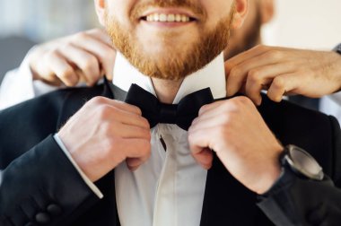 Damat düğünde boynuna papyon takar ve arkadaşı ona yardım eder. Düğün konsepti. Moda, tarz, yaşam tarzı. İş adamı kılığına girmiş..