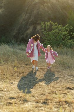 Genç bir anne ve kız aynı güzel süveterlerle dağların arasında yürüyorlar. Aktif dinlenme ve akşam günbatımı neşenizi arttırır.