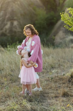 Genç bir anne ve kız aynı güzel süveterlerle dağların arasında yürüyorlar. Aktif dinlenme ve akşam günbatımı neşenizi arttırır.