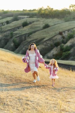 Genç bir anne ve kız aynı güzel süveterlerle dağların arasında yürüyorlar. Aktif dinlenme ve akşam günbatımı neşenizi arttırır.