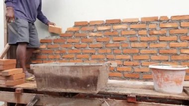 Bir inşaatçı duvar örmek için betonla tuğla düzenlemeye çalışıyor.