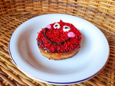 Gülümseyen bir simgeye benzeyen kremalı ve serpilmiş bir çörek.