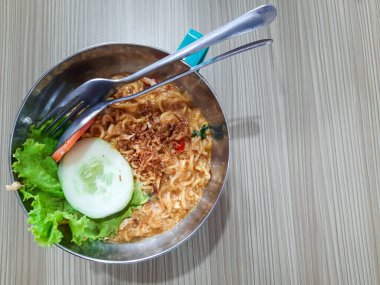 Mie Goreng 'in üst görüntüsü veya yumurta, salatalık ve hardal yeşili lezzetli kızarmış erişteler, paslanmaz çelik kasede servis edilir. Endonezya fast food