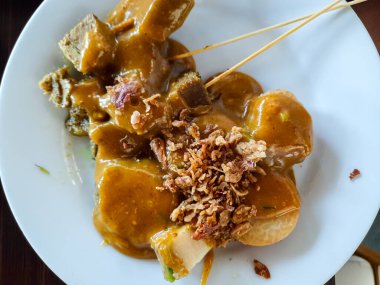 Endonezya sığır eti satay şiş yakın çekim zengin fıstık sosu ile servis, üzerinde beyaz bir tabakta kızarmış arpacık soğanı. Popüler Güneydoğu Asya sokak yemekleri.