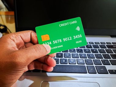 İçinde gömülü bir çip ve temassız ödeme sembolü olan yeşil bir kredi kartı tutuyor. Çevrimiçi alışveriş kavramı, dijital ödemeler ve e-ticaret