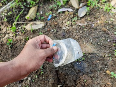 Yerden atılan plastik şişeyi, çevresel temizliği, atık yönetimi ve çevre dostu uygulamaları toplayan bir el.