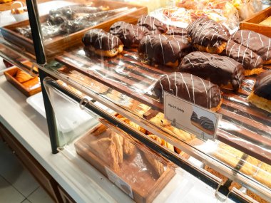 Bir cam fırın vitrininde üzerinde fiyat etiketi olan çikolata kaplı pastalar. Endonezya pazarında parlak çikolata kaplı tatlı ikramları