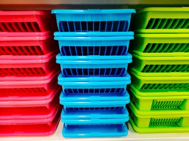 Renkli plastik sepetler, kırmızı, mavi ve yeşil sepetler düzgünce bir rafa dizilmiş. Ev veya ofis eşyalarının düzenlenmesi için ev içi depolama konteynerleri