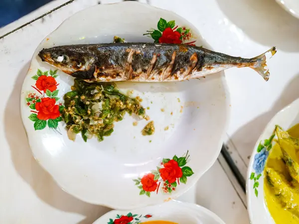 Klasik çiçek desenli diş mineli tabakta baharatlı yeşil biberli sambal ile servis edilen ızgara balığın yakın çekimi. Geleneksel Batı Sumatra mutfağı, Endonezya