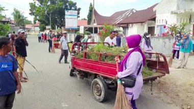 Pariaman, Endonezya - 28 Mayıs 2025: Naras Hilir köyündeki bir sokak temizleme çalışması sırasında vatandaşlar üç tekerlekli bir karavana kesilmiş yaprak ve ot yüklüyorlar