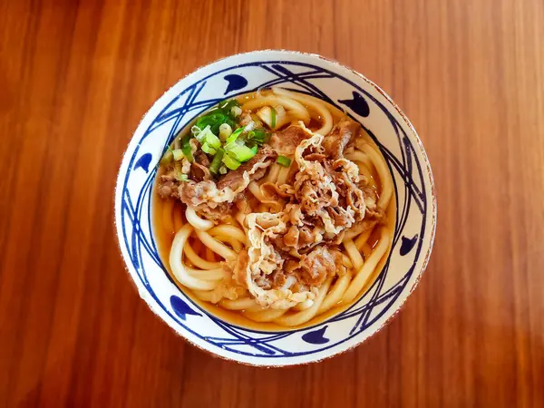 Niku Udon 'un üst görüntüsü, dilimlenmiş sığır eti ve lezzetli et suyuyla Japon erişte çorbası. Geleneksel konforlu yemekler tatlı, tuzlu ve umami aromalı.