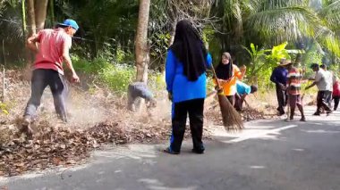 Pariaman, Endonezya - 25 Haziran 2025: Sungai Rambai 'deki bir toplum temizliği sırasında köy temizlik işçileri yol kenarındaki aşırı büyümeyi temizledi