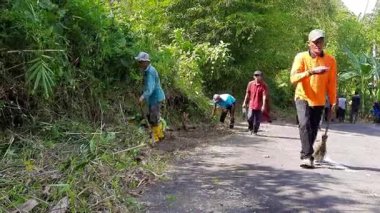 Pariaman, Endonezya - 25 Haziran 2025: Sungai Rambai 'deki köy temizlik işçileri, Kuzey Pariaman' daki dönüşümlü temizlik girişimi sırasında yol kenarını temizledi