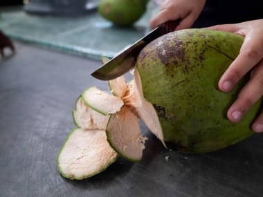 İçi hindistan cevizi suyuyla dolu olan iç kabuğa ulaşmak için büyük bir bıçakla genç bir hindistan cevizini soyan birinin yakın çekimi. Geleneksel tropikal meyve hazırlama