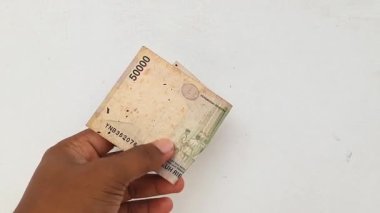 Beyaz arka planda izole edilmiş modası geçmiş Endonezya rupia banknotlarını tutan bir el. Bu eski para birimi notları artık satışta veya işlemler için geçerli değil