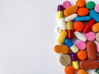 Sağ tarafta beyaz arka plan ve kopyalama alanı ile düzenlenmiş çeşitli renkli kapsüller ve tabletler. Eczacılık ve sağlık hizmetleri kavramı izole edildi