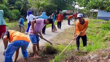 Pariaman, Endonezya - 23 Haziran 2025: Kuzey Pariaman 'daki dönüşümlü temizlik girişimi sırasında köy temizlik işçileri Manggung' daki yol kenarındaki ot ve otları temizledi.
