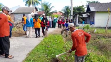 Pariaman, Endonezya - 23 Haziran 2025: Erkekler yolu genişletmek için çapaları kullanarak asfalt bir yolun kenarını temizler. Manggung köyündeki yol kenarını kaplayan toprak ve çimenleri temizliyorlar..