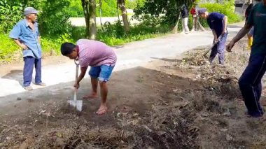 Pariaman, Endonezya - 23 Temmuz 2025: Erkekler Manggung Köyü 'ndeki bir köy temizliği sırasında yol kenarını temizlemek için çapa ve kürek kullanıyor