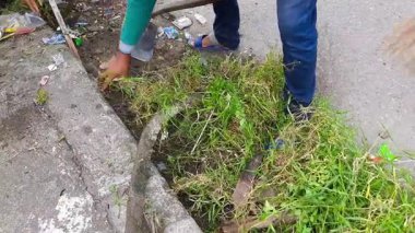 Endonezya 'nın Pariaman kentindeki bir topluluğun temizliğinin bir parçası olan çapa kullanarak yol kenarındaki otları ve plastik atıkları temizleyen bir adamın yakın çekimi.