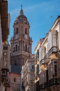 Malaga Cathedral's north tower built in Gothic, Renaissance, and Baroque style captured from a narrow street bustling with locals and tourists