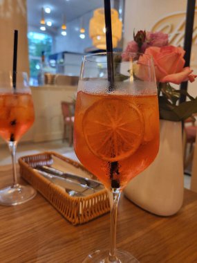 Pembe güllerin yanında buz ve portakal dilimli Aperol, mükemmel bir besin ve içecek kompozisyonu..
