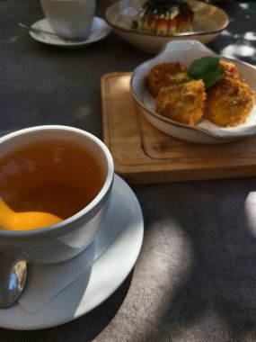  Dışarıdaki ahşap bir tahtada sunulan sıcak bir çay ve küçük bir tatlı.