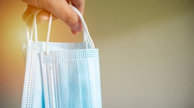 Mavi maske tutan eller ya da solf hafif arka planda bej üzerinde tıbbi maskeler. Koruma kavramı