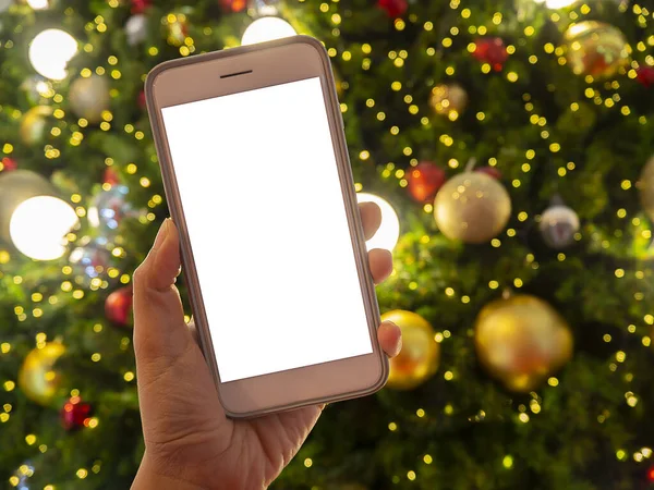 Close up of woman holding phone with empty white screen mockup near decorated festive tree, celebrating Christmas, customer shopping online, purchasing gifts, browsing gadget apps