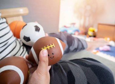 Kanepede oturan, elinde bir sürü top tutan, evde oyuncak oynayan Asyalı çocuğun tıkanmış görüntüsü..