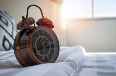 Yatak odasındaki beyaz yatağa takılmış antika bir çalar saati kapat. Yumuşak bir güneş ışığı yan pencereden içeri girsin..